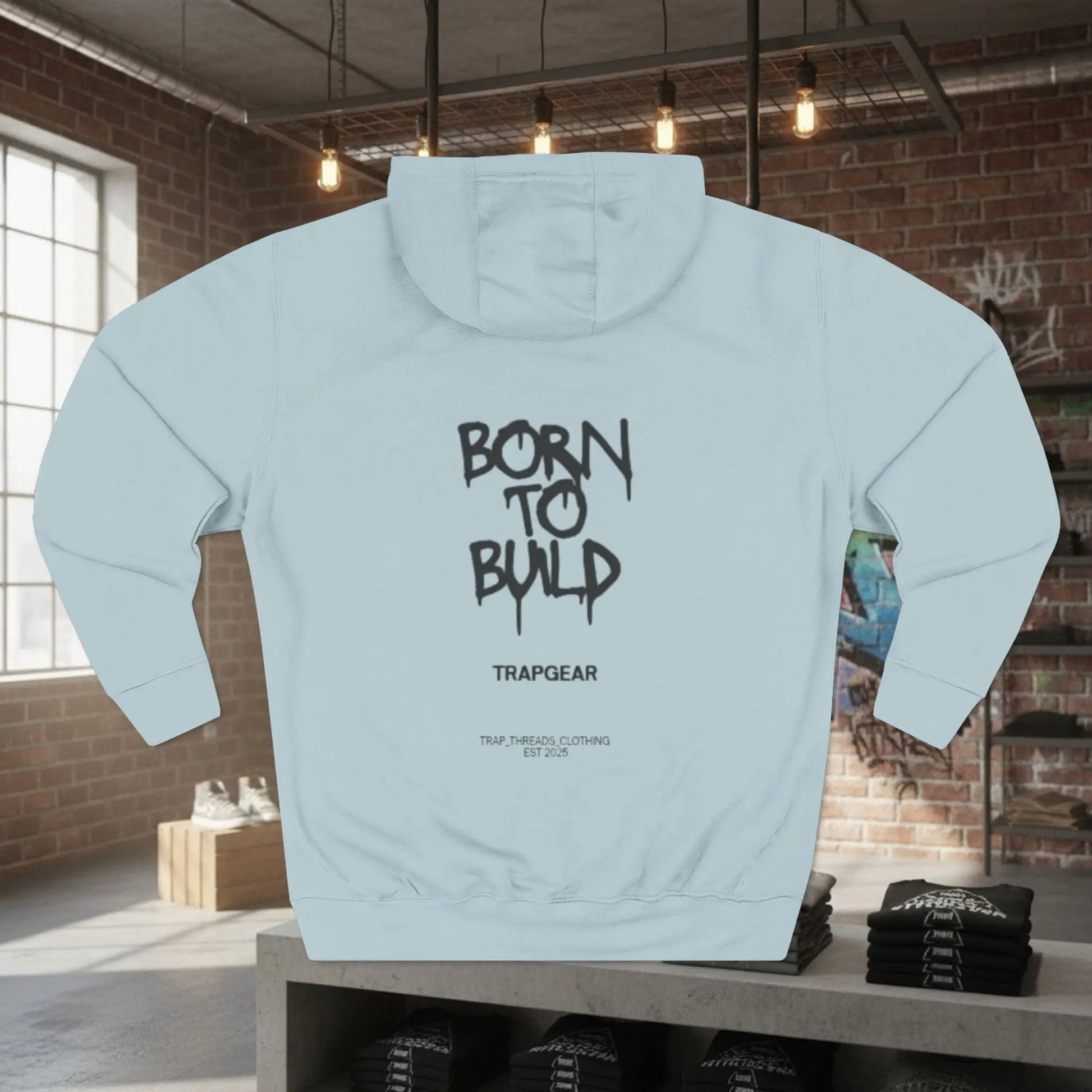 Light blue hoodie with 'Born to Build' text on the back, displayed in a room with brick walls and windows.